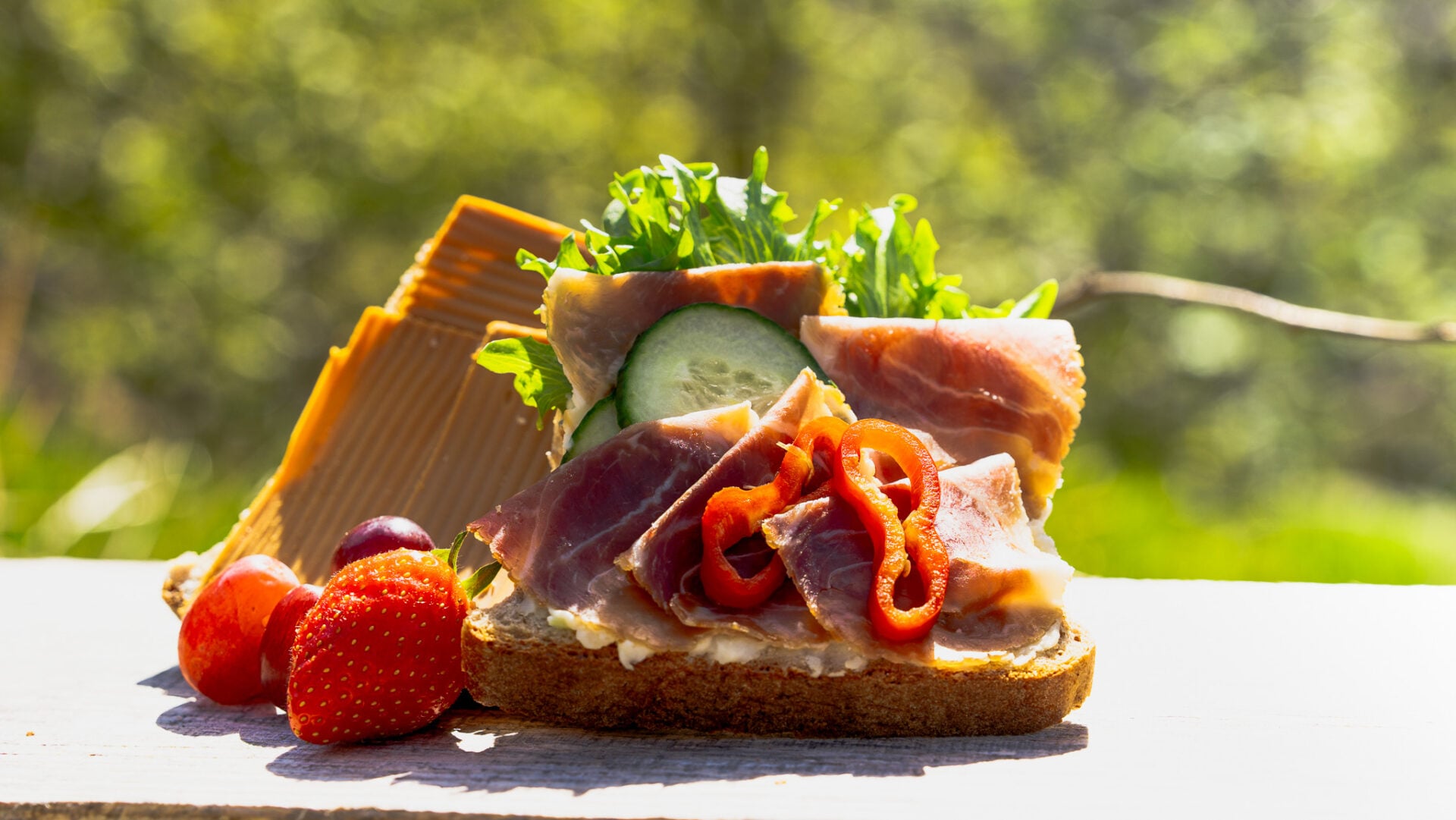 Fresh Norwegian lunch served during a guided waterfall hike in Rosendal on a day trip from Bergen, featuring local cured ham, brown cheese, crisp vegetables and berries surrounded by nature in Hardangerfjord.
