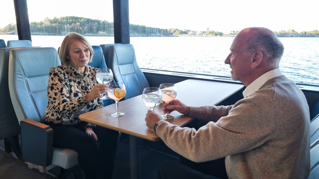 Ektepar nyter ginsmaking i salongen på fjordcruise fra Stavanger, med to ulike gin-varianter foran seg.