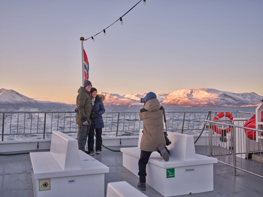 Et par som blir tatt bilde av på fjord cruise i Tromsø med vakker sol som lyser over fjellene i bakgrunnen.