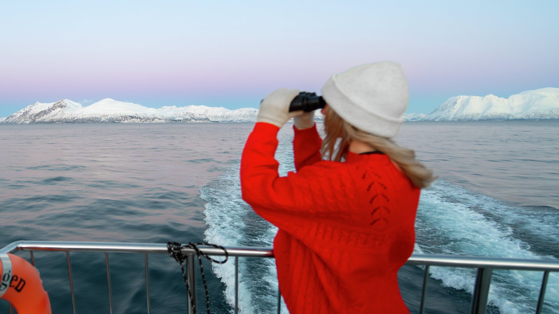 Girl in red knitted jumper looking at the Arctic landscape on a fjord cruise from Tromsø through a binocular