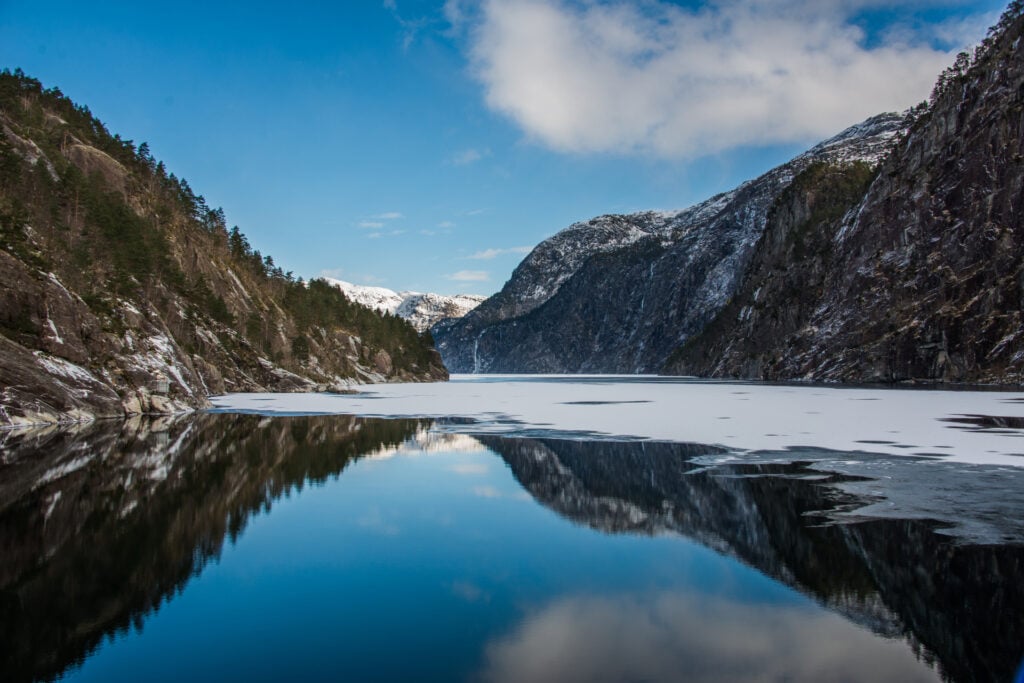 Breathtaking view of a fjord with icy water and snow-dusted mountains, capturing the raw beauty of Norway in winter.