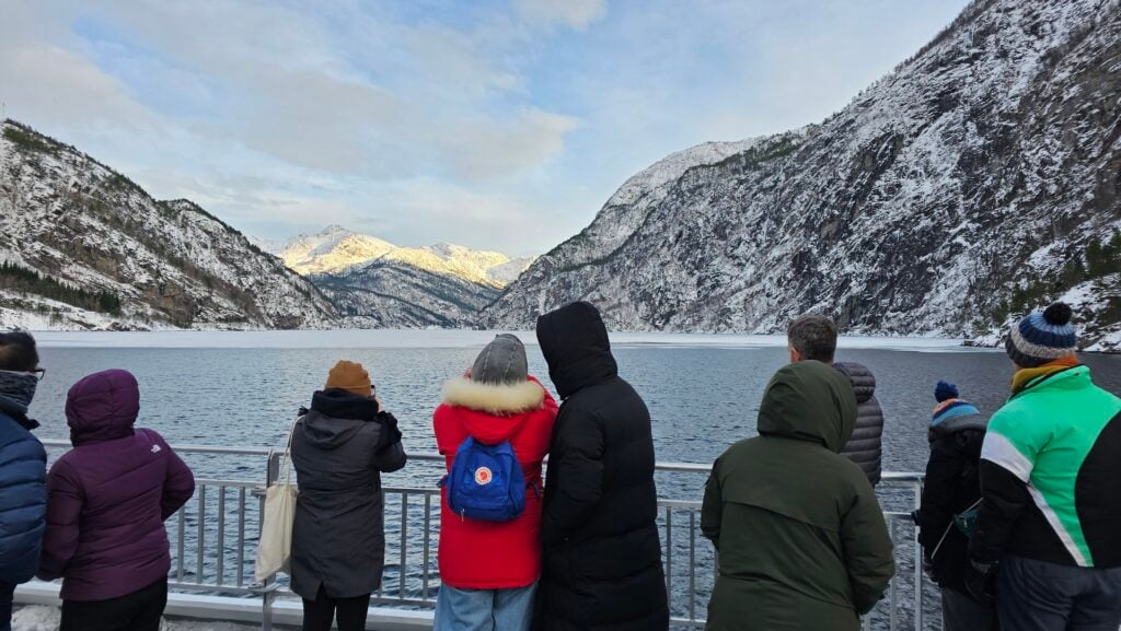 Passengers on deck during winter fjord cruise in snowy Norwegian mountains