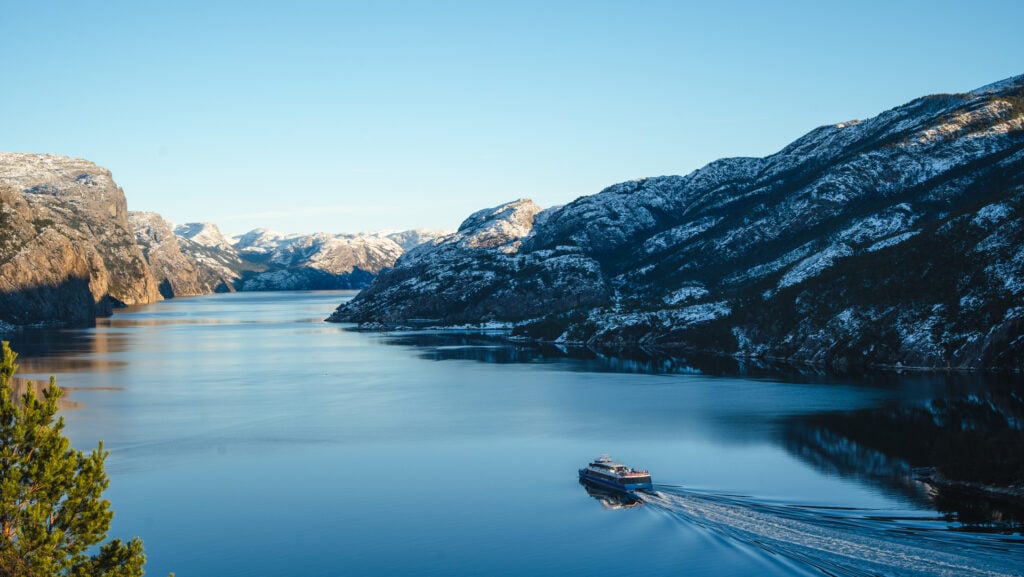 Fjord cruise boat sailing through the Lysefjord in winter surrounded by snow-covered mountains