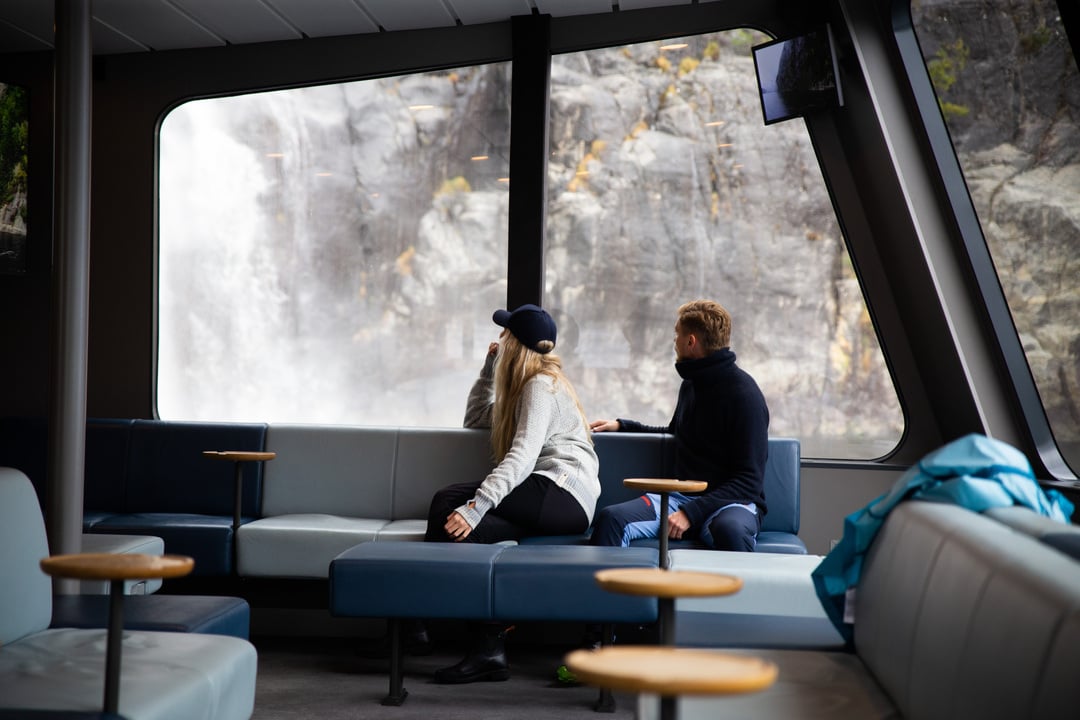 To passasjerer nyter utsikten over Lysefjorden fra loungen på et moderne fjordcruise.