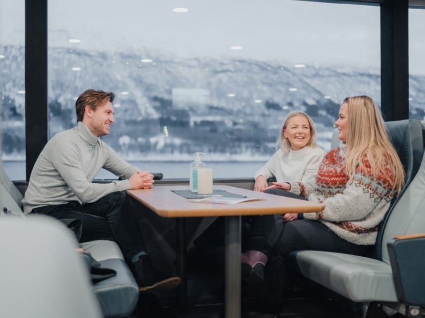 Gjester nyter utsikten over de arktiske fjordene fra salongen på et bærekraftig fjordcruise i Tromsø.