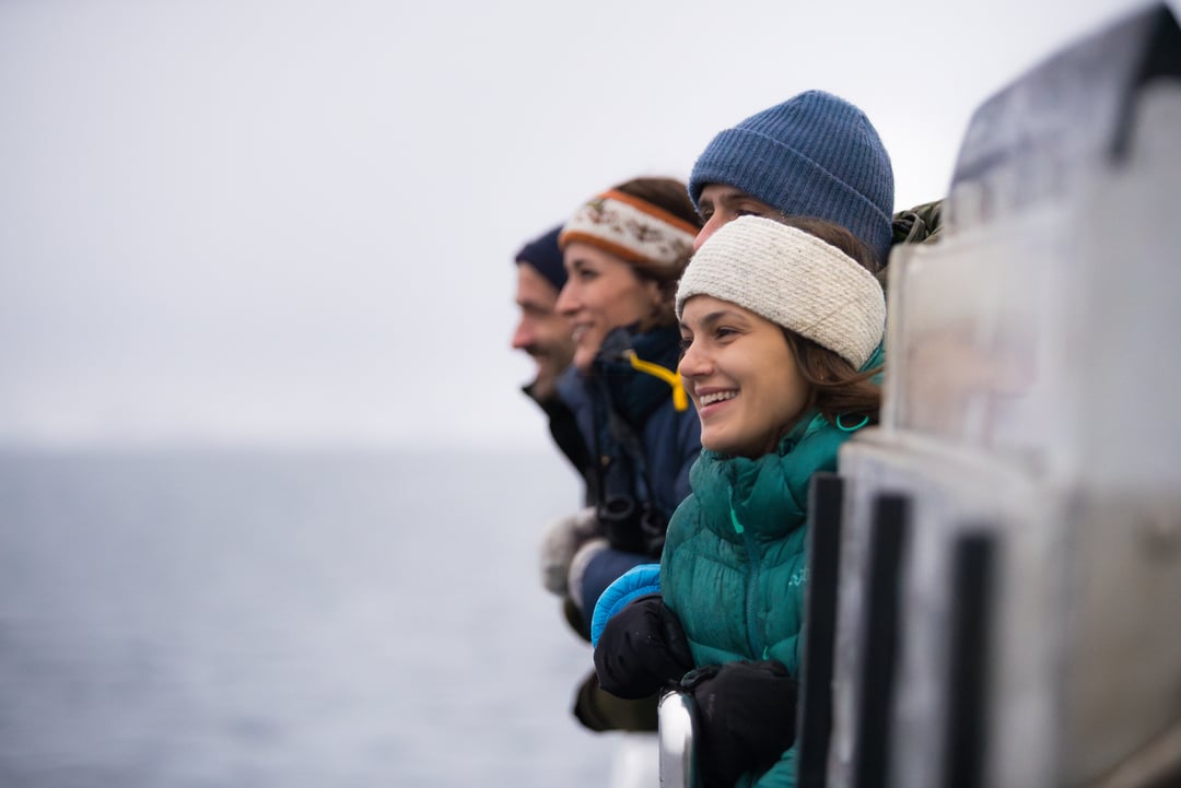 Gjester nyter utsikten over de arktiske fjordene i Nord-norge fra dekk på et bærekraftig fjordcruise i Tromsø.