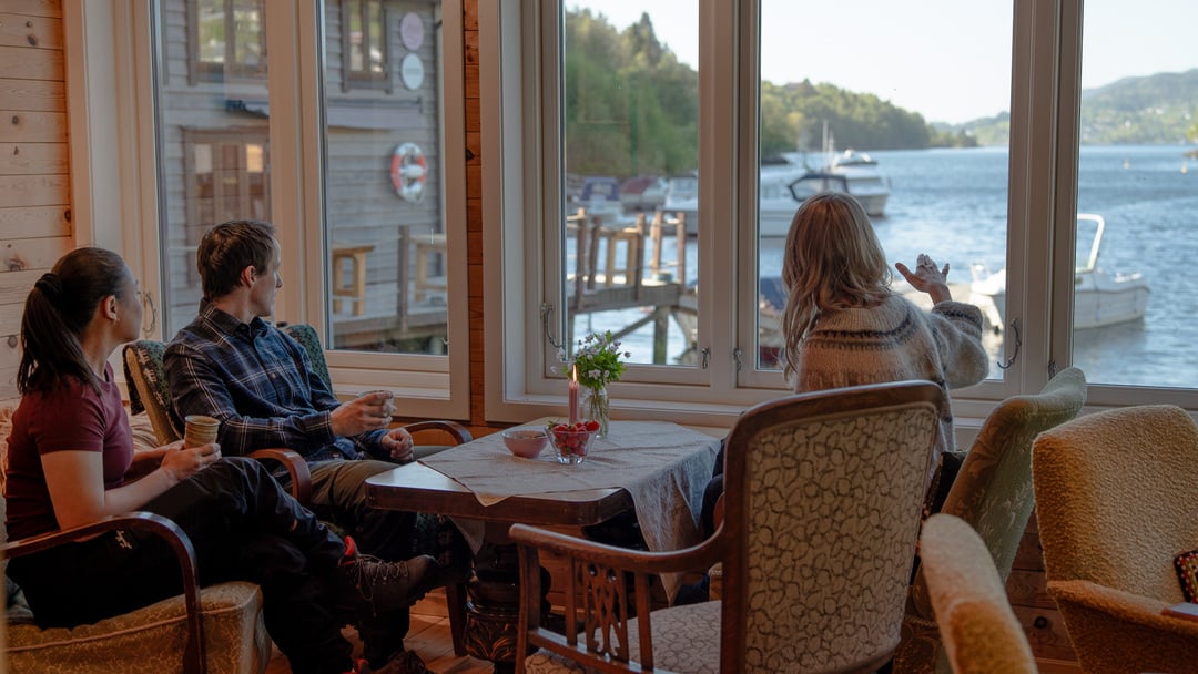 Guests enjoying coffee inside a cozy waterfront cabin overlooking a Hosanger and Osterfjord near Bergen, Norway