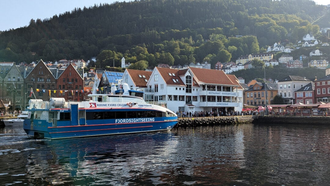 Rødne Fjord Cruise-båt ved Bryggen i Bergen med historiske trehus i bakgrunnen og passasjerer langs kaien på vei til strikkebåt til Salhus