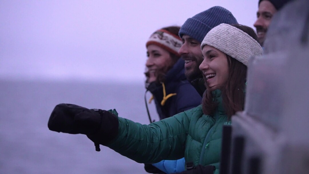 A woman smiling and pointing towards the whales surfacing just outside the boat on a Whale safari in Northern Norway