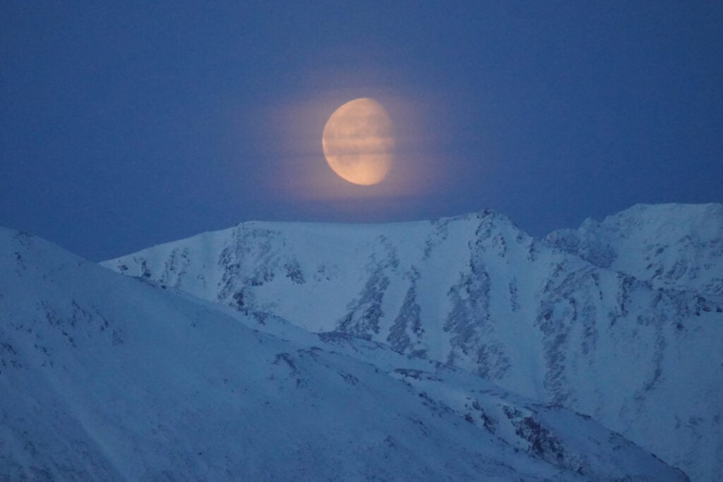 The Moon rising above the peaks of Lyngen Alps in Northern Norway, highlighting Arctic mountain landscapes at polar night.