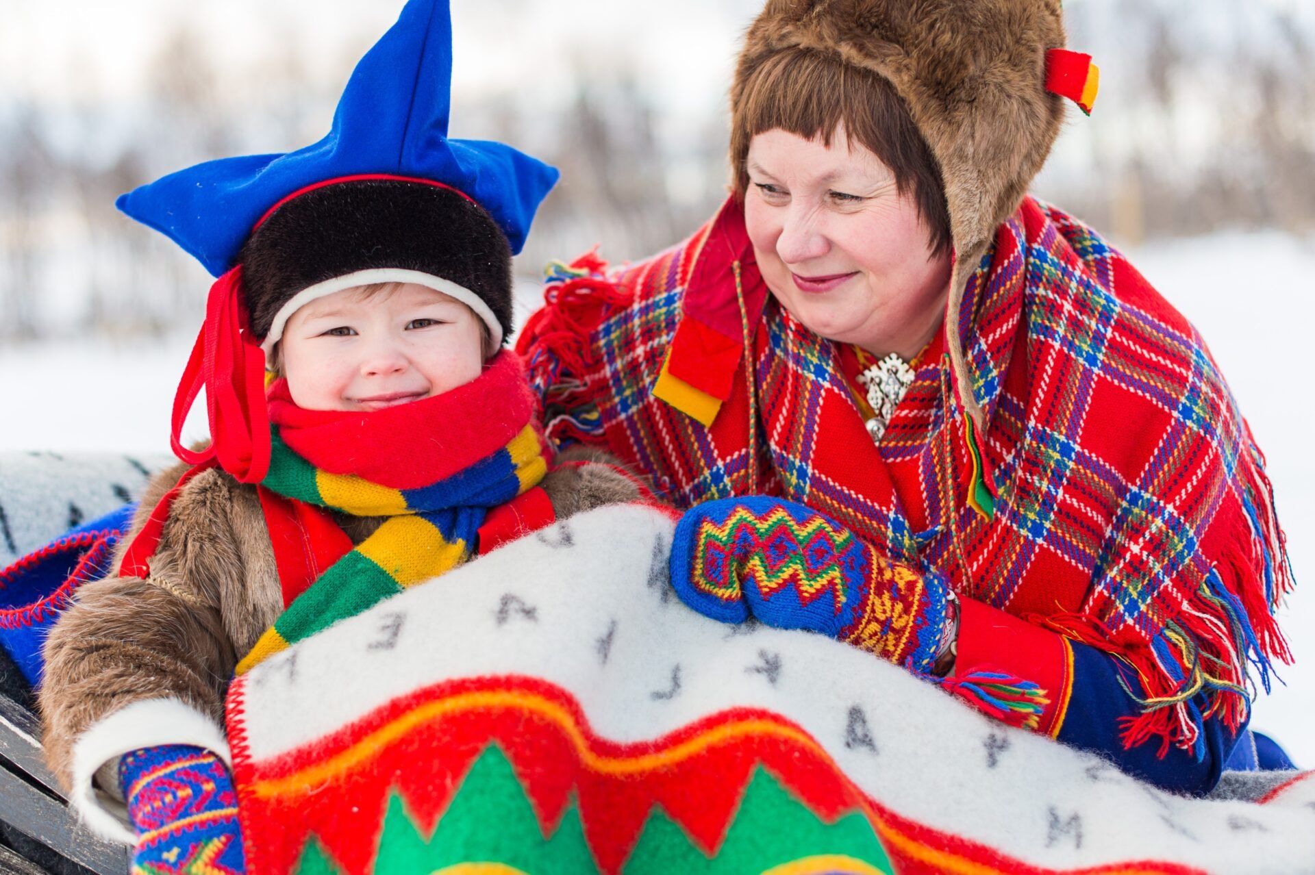 Sami grandmother and grandchild dressed in traditional gákti clothing, standing under the Arctic sky in Northern Norway.