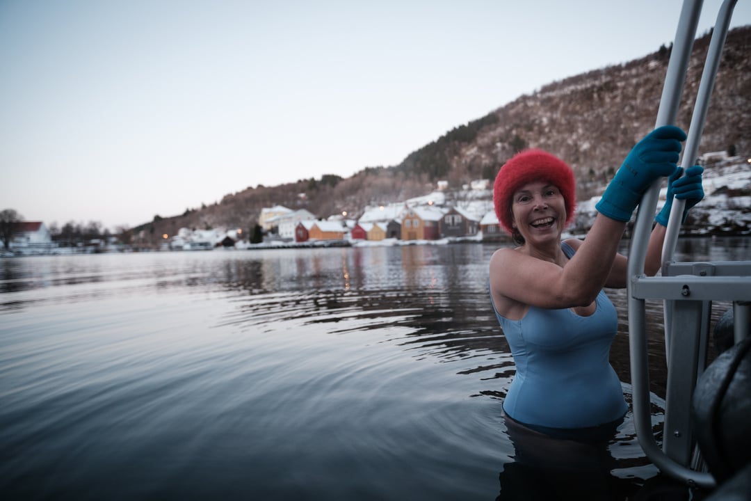 Woman winter swimming in cold sea water in Bergen surrounded by snowy landscape