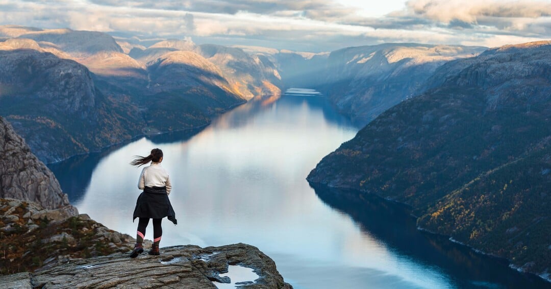Person steht auf dem Preikestolen und blickt über den Lysefjord und die umliegende Fjordlandschaft