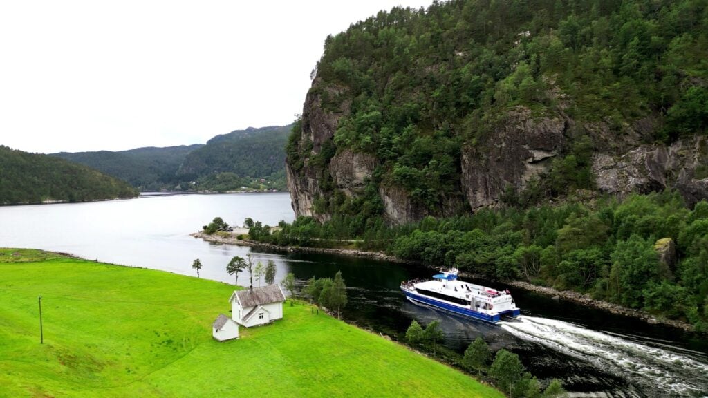 Båt på fjordcruise i Mostraumen omgitt av fjell, skog og grønt landskap