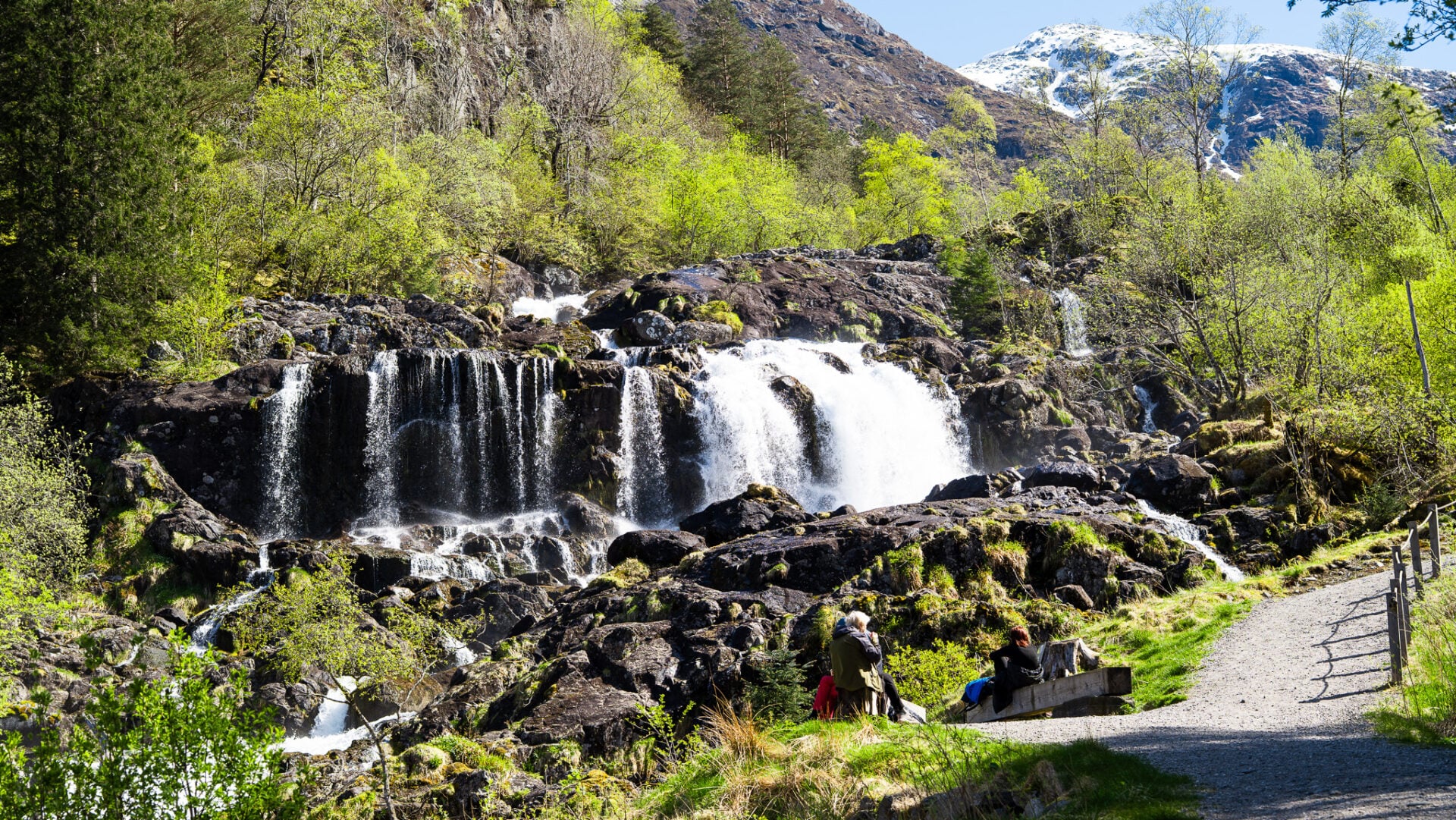Travelers relaxing beside a waterfall in Rosendal during a guided hike and fjord day trip from Bergen in Hardangerfjord.