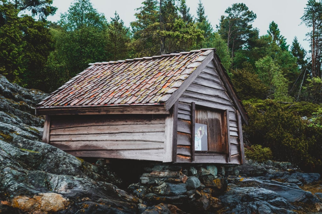 Gammel trehytte med tegltak på svaberg omgitt av skog vest for Bergen.