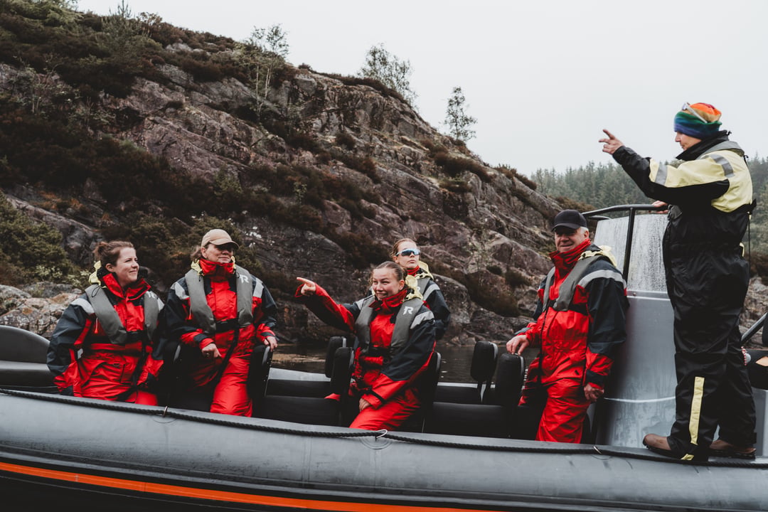 Rødne guide pointing out the landscape to seated guest on a RIB west of Bergen.