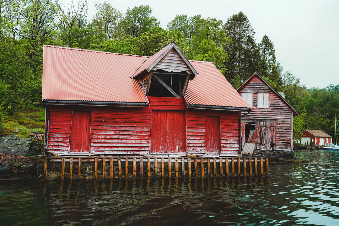 Weathered red wooden boathouse at the water's edge among the islands west of Bergen.