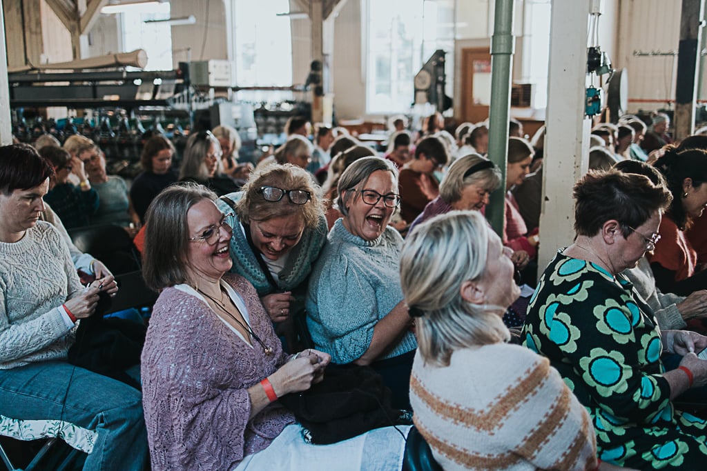 Mange kvinner som koser seg, strikker og ler inne i lokalene til Trikotasjemuseet i Salhus. De deltar på Bergen Strikkefestival og hører på et foredrag mens de strikker.